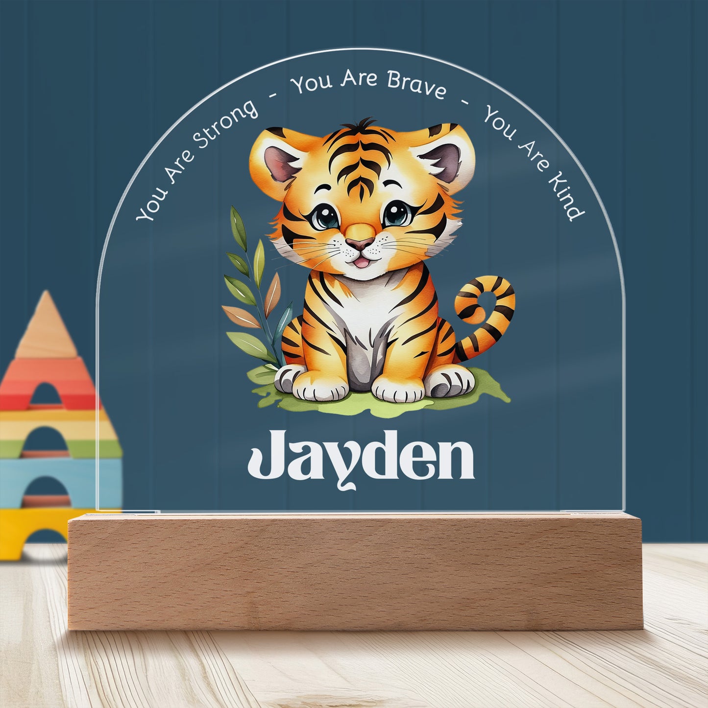 Adorable Tiger Cub Personalized Night Light with Battery powered base featured on a light timber table with a dark blue panelled wall and child's building block toy in the background.