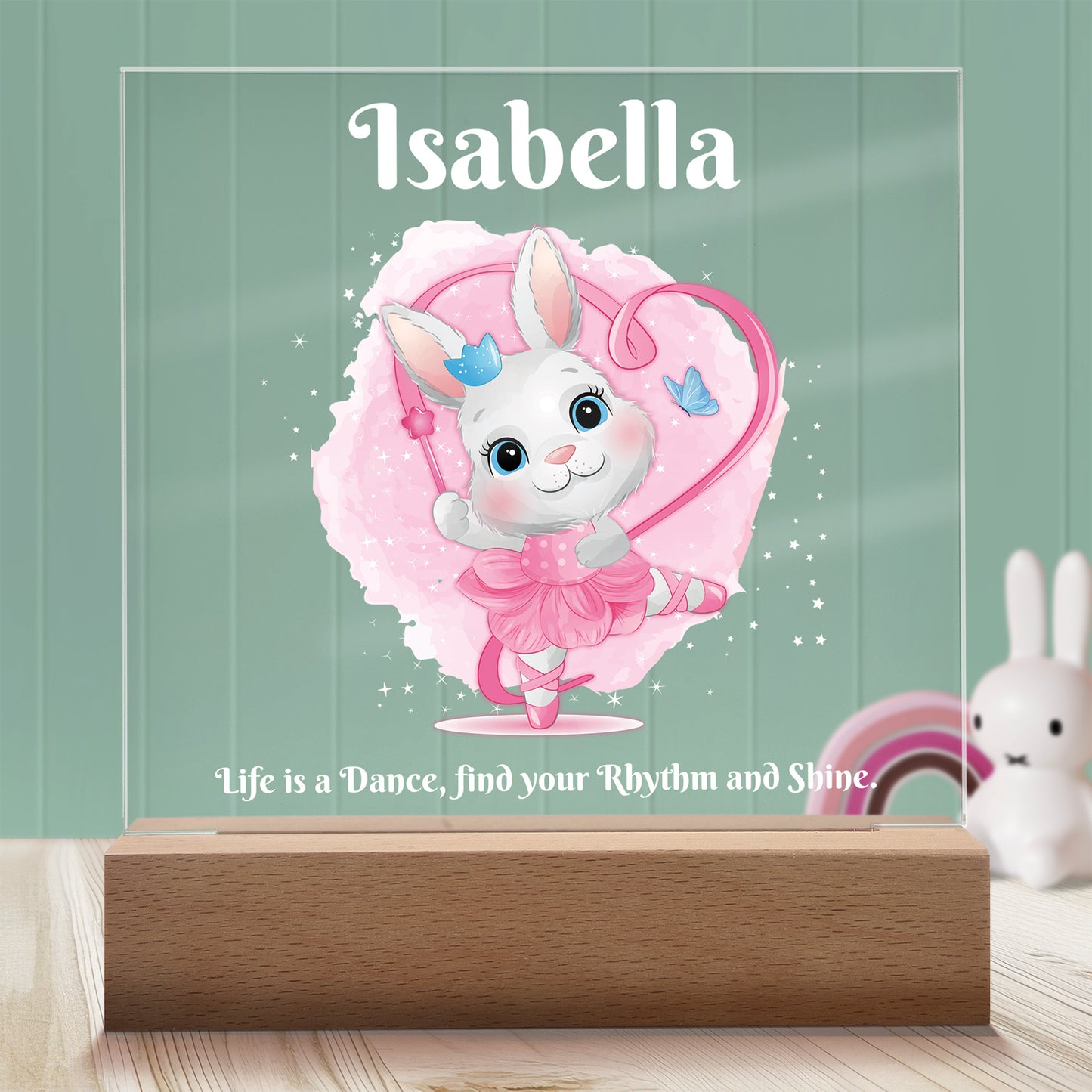 Dancing Bunny Personalized Night Light with Battery powered base featured on a light timber table with a mint green panelled wall and bunny and rainbow ornaments in the background.