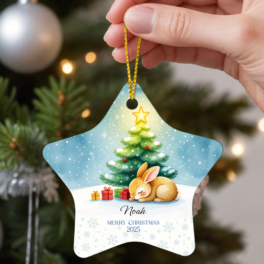 Star-shaped Personalized Christmas ornament with a sweet bunny sleeping and tree design, held by a hand in front of a decorated tree.