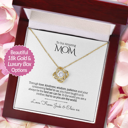 Beautiful Love Knot necklace in 18k Gold finish with a round-cut cubic zirconia in the center, presented in a luxury mahogany-style gift box with a personalized message card to Mom, on a background of soft pink rose petals.