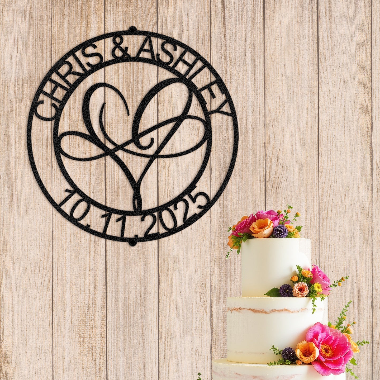 Infinite Love Personalized Metal Decor in Black customized with names and date next to a wedding cake with flowers on a wooden background.