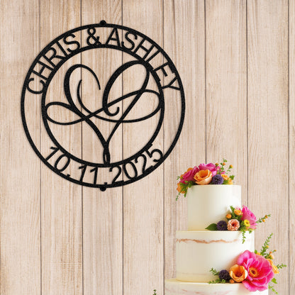 Infinite Love Personalized Metal Decor in Black customized with names and date next to a wedding cake with flowers on a wooden background.