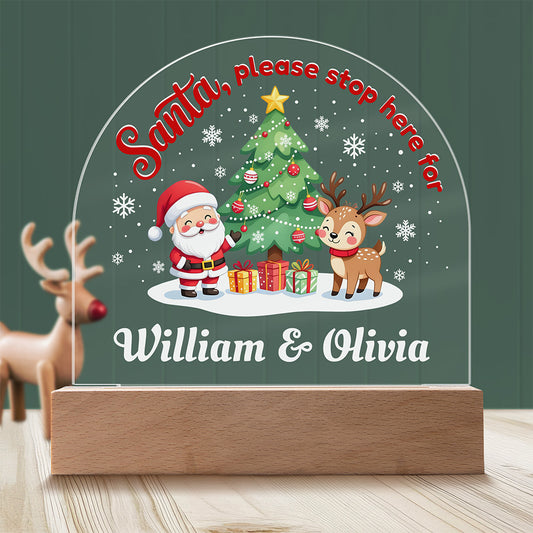 Decorative sign with Santa, reindeer, and Christmas tree on a wooden base against a green background.