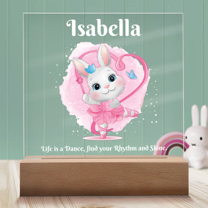 Dancing Bunny Personalized Night Light with Battery powered base featured on a light timber table with a mint green panelled wall and bunny and rainbow ornaments in the background.