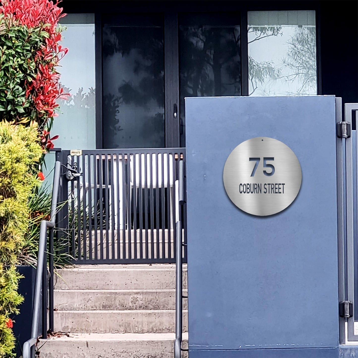 Contemporary Circle Address Metal Sign displayed in Silver, mounted on a modern blue plaster wall facing the street.