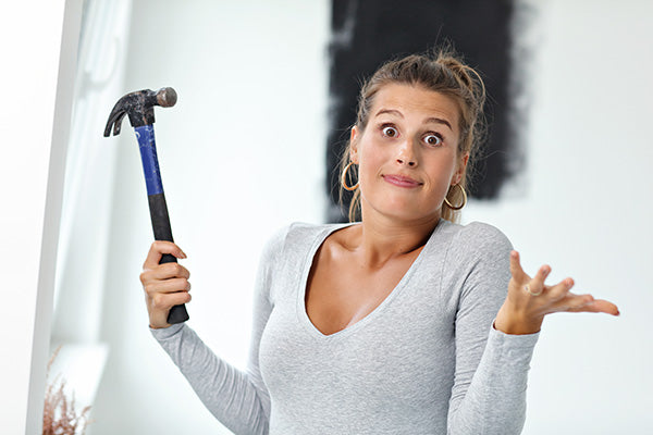Woman expressing confusion while holding a hammer wondering about the best way to hang her Metal Decor.